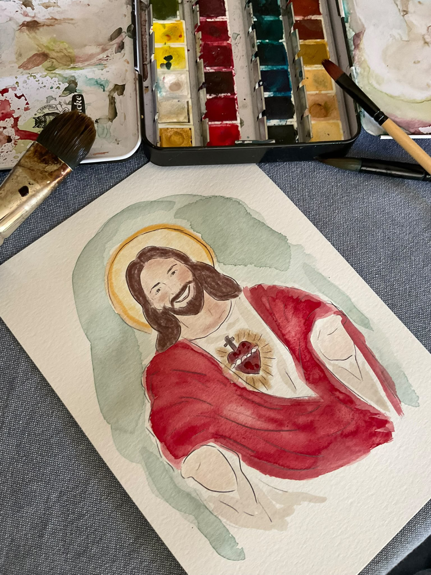 Fotografía de una acuarela del Sagrado Corazón de Jesús junto a una paleta y pinceles