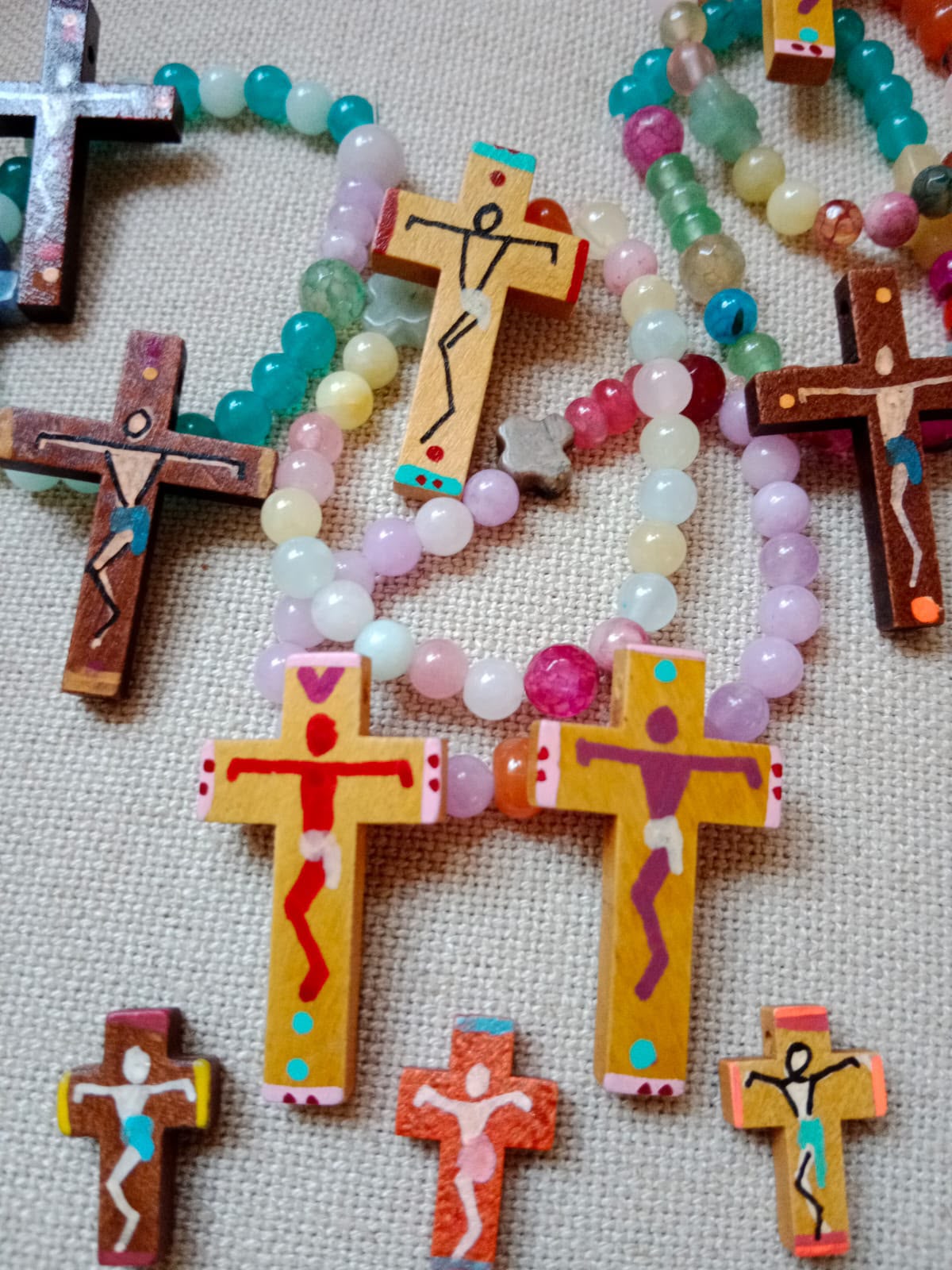 Fotografía de cruces de madera pintadas con figuras de Jesús y rodeadas de cuentas de colores