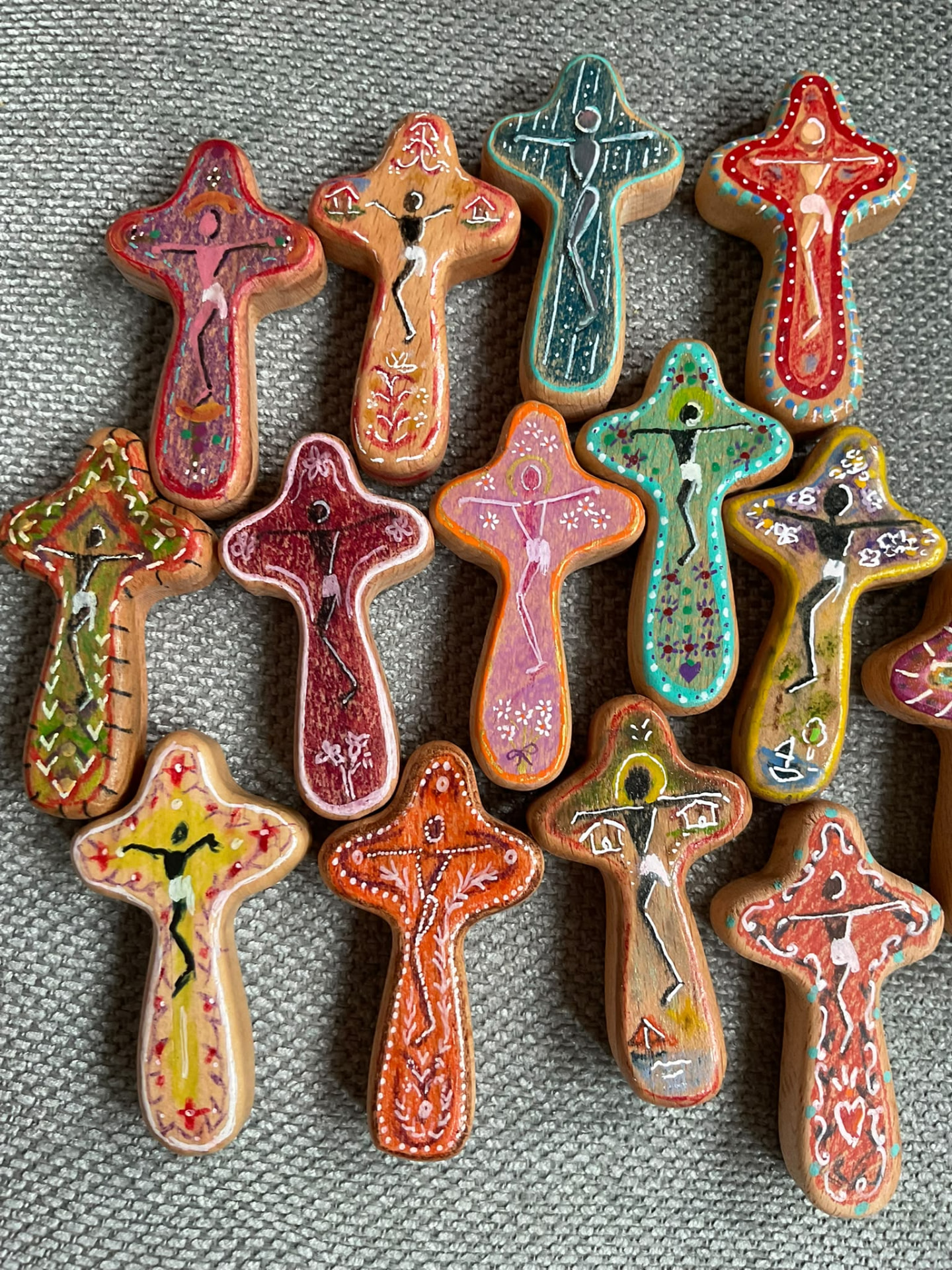 Detalle de cruces de madera pintadas a mano en distintos colores sobre una tela gris
